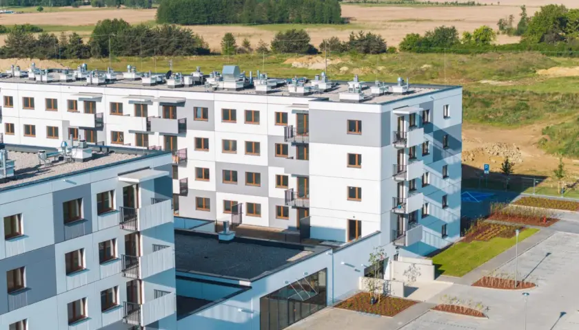 Nowa winnica Miękinia: nowoczesne bloki mieszkalne z balkonami, otoczone zielenią i parkingiem, na tle pól i lasu.