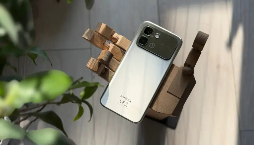 Srebrny smartfon Infinix, marka znana z innowacyjnych rozwiązań, prezentuje się na drewnianej dłoni.