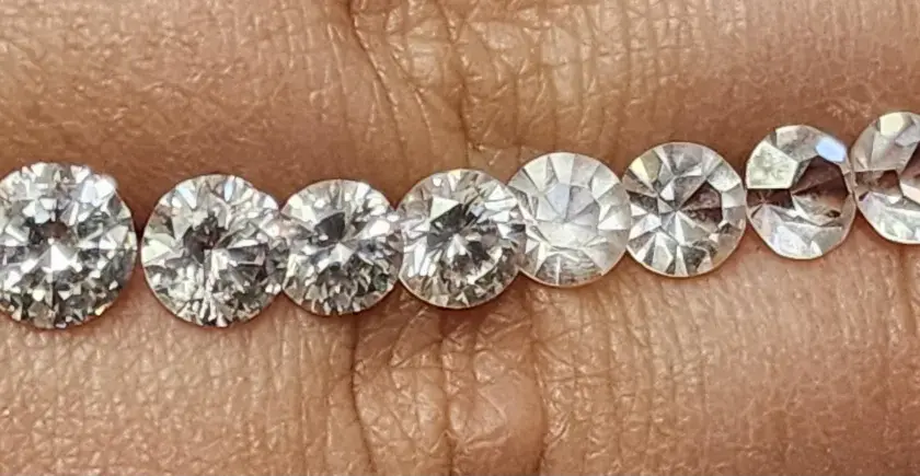 Reihe von geschliffenen Steinen, die auf einer Hautoberfläche liegen. Es ist schwierig, diamant oder zirkonia erkennen, da sie sehr ähnlich aussehen.