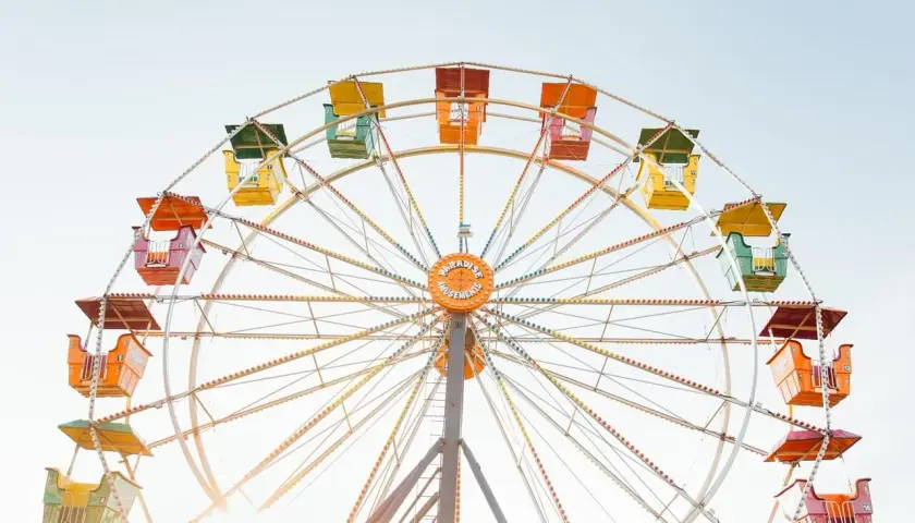Grande roue colorée avec des nacelles jaunes, vertes, oranges et rouges sous un ciel clair.