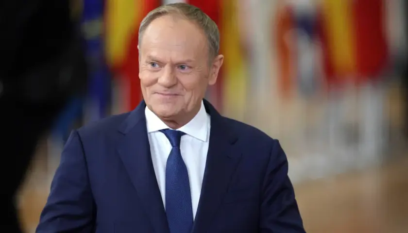 Uśmiechnięty Donald Tusk w granatowym garniturze i białej koszuli z niebieskim krawatem. Dziś Tusk robi wrażenie zadowolonego.
