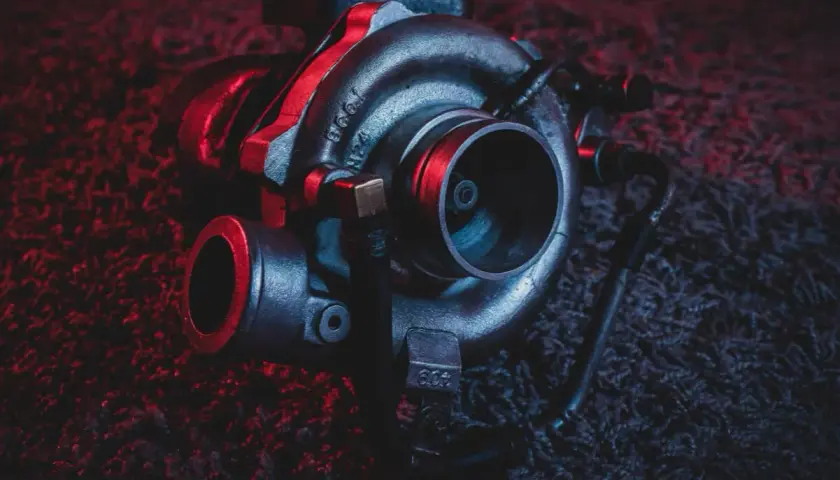 Turbosprężarka po regeneracji, gotowa do montażu. Ciemne tło z czerwonymi akcentami podkreśla jej moc.