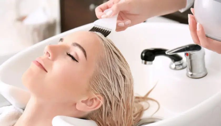 Kobieta z blond włosami w salonie fryzjerskim, gdzie nakładany jest jej kolor.