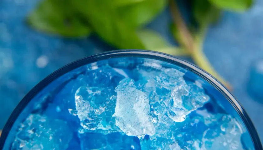 Intensywnie niebieski likier Blue Curacao z kruszonym lodem w szklance, z zielonym liściem w tle.