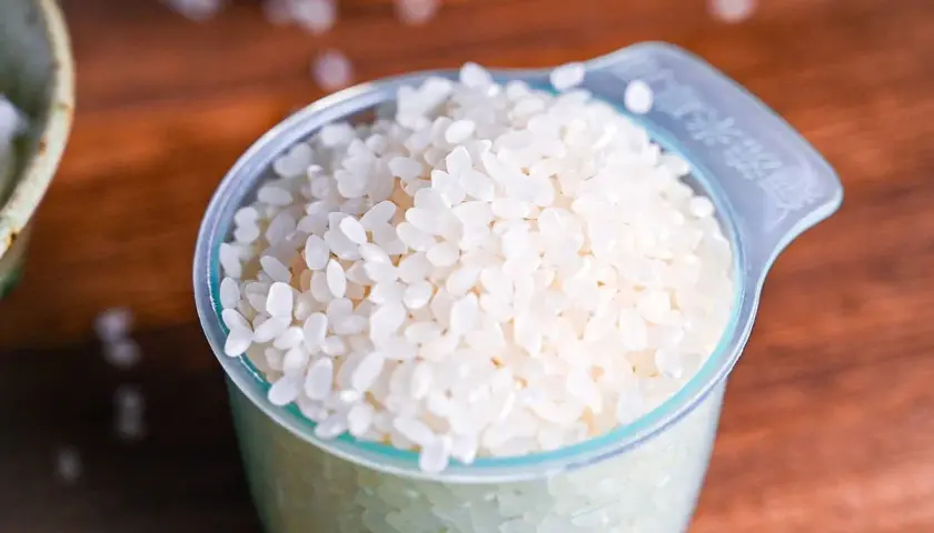 A measuring cup filled with short-grain white rice, ready for cooking Japanese rice.