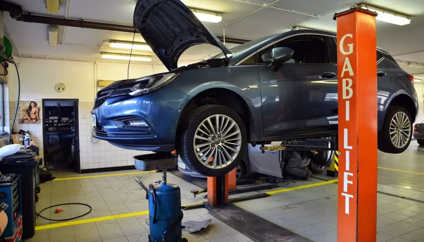 Samochód na podnośniku w warsztacie, mechanik sprawdza ile za wymianę oleju i filtra.