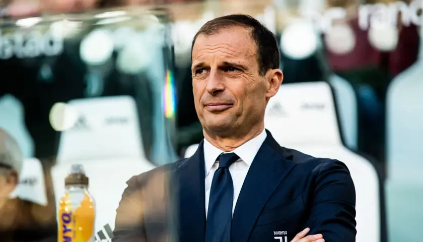 Massimiliano Allegri, w eleganckim garniturze, z rękami skrzyżowanymi na piersi, obserwuje grę.