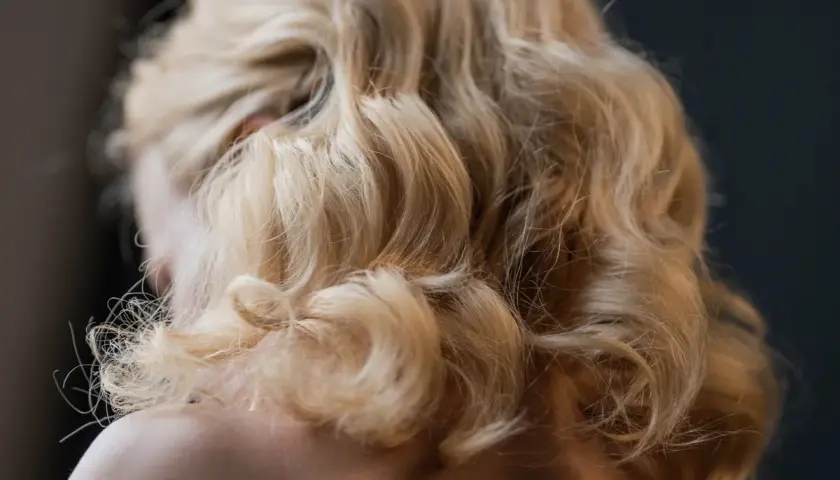 Blond włosy ułożone w eleganckie fale, tworzące fryzurę w stylu retro.