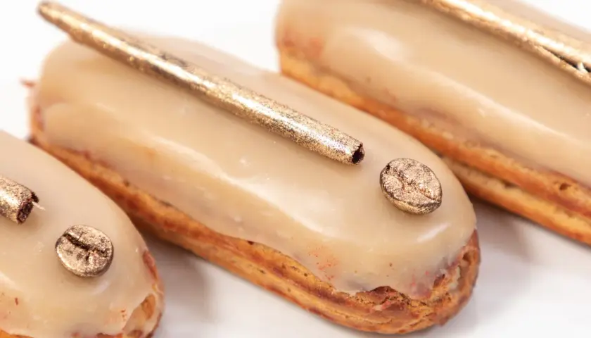 Délicieux éclairs au café, parfaits pour savoir quoi faire avec de la crème pâtissière. Ils sont décorés de grains de café dorés et d'une touche de paillettes.