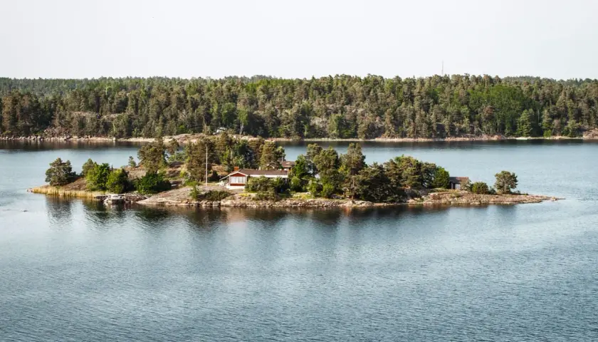 Malutka wyspa z domkiem i drzewami, część archipelagu sztokholmskiego, otoczona spokojną wodą.