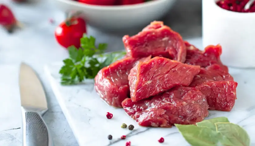 Morceaux de viande rouge crue sur une planche en marbre, avec des tomates cerises et des herbes. Question : viande hors frigo combien de temps ?
