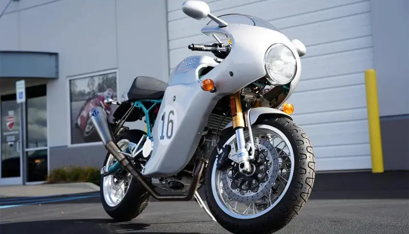Moto Ducati plateada con el número 16, inspirada en el estilo de Paul Smart, lista para la carretera.
