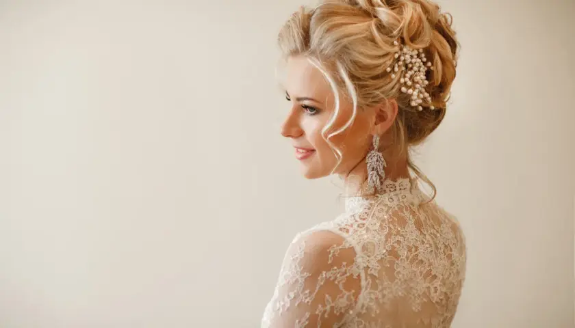 Elegancka panna młoda z upiętymi włosami ozdobionymi perłami i kryształami. Jej fryzury ślubne glamour podkreślają delikatne loki opadające na ramiona.