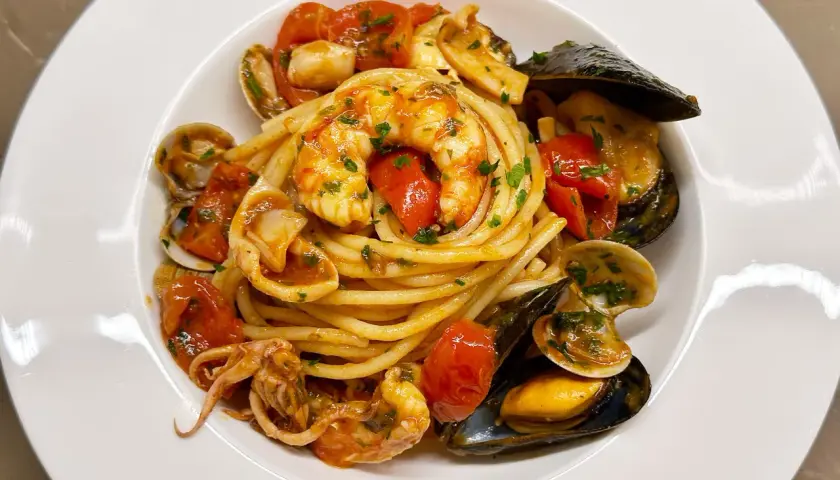 Un invitante piatto di spaghetti allo scoglio, con gamberi, cozze, vongole e calamari, condito con pomodorini e prezzemolo.