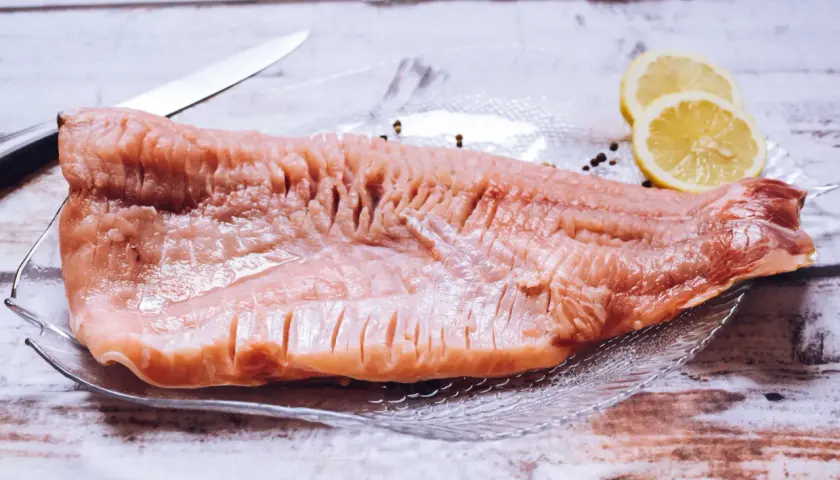 Surowy filet karpia na talerzu z cytryną i pieprzem, obok nóż.