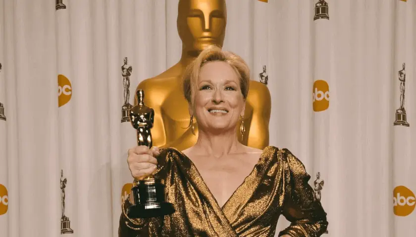 Meryl Streep z Oscarem, aktorka, która zdobyła najwięcej oscarów w XXI wieku, pozuje na tle złotych statuetek.