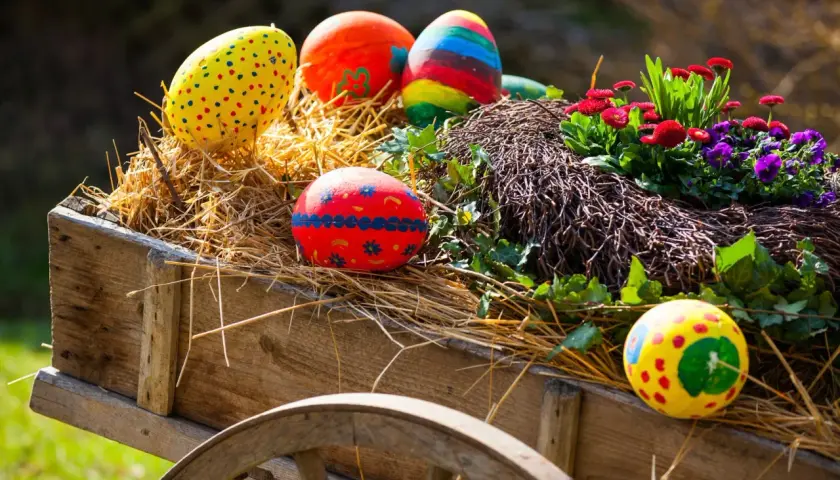 Bunte Ostereier und Blumen schmücken einen alten Wagen, perfekt für Ostermontag Veranstaltungen.