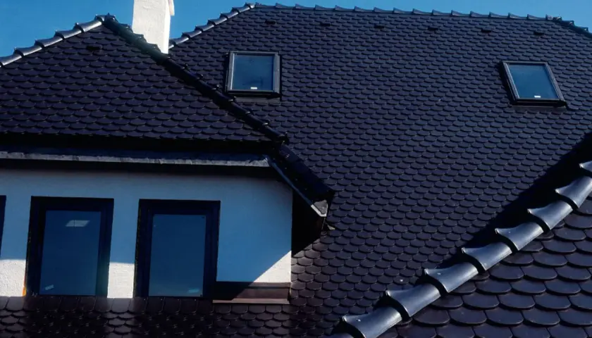 Ciemny dach z dachówki ceramicznej, z kominem i oknami dachowymi. Zastanawiasz się, ile waży paleta dachówki ceramicznej?