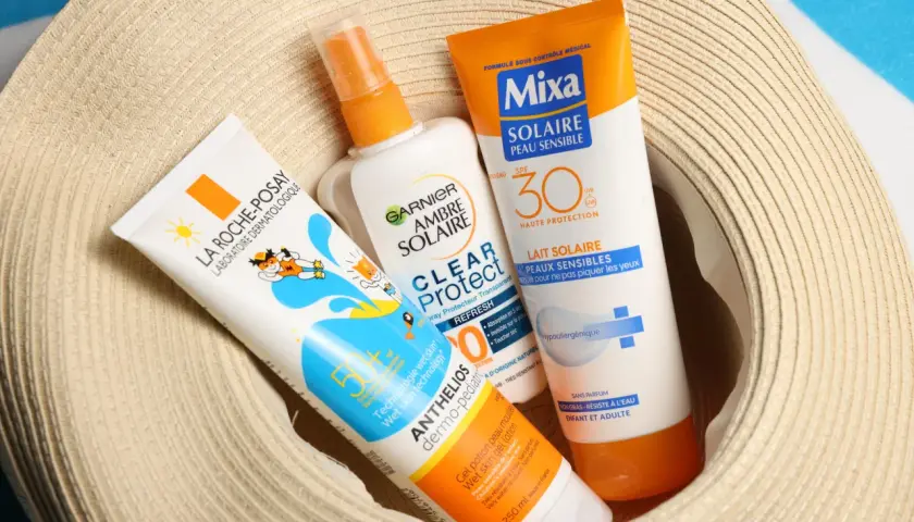 Trois tubes de crème solaire, dont une crème solaire périmée, sont posés sur un chapeau de paille.