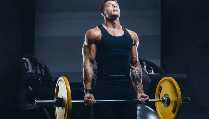 Mięśniowy mężczyzna wykonuje ćwiczenie na biceps z ciężarem. Jego **split trening** przynosi efekty.