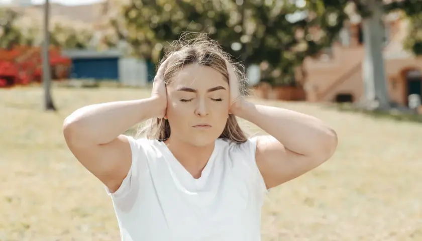 Ragazza con le orecchie tappate, occhi chiusi, espressione di ansia. Il rumore del mondo esterno è troppo forte.