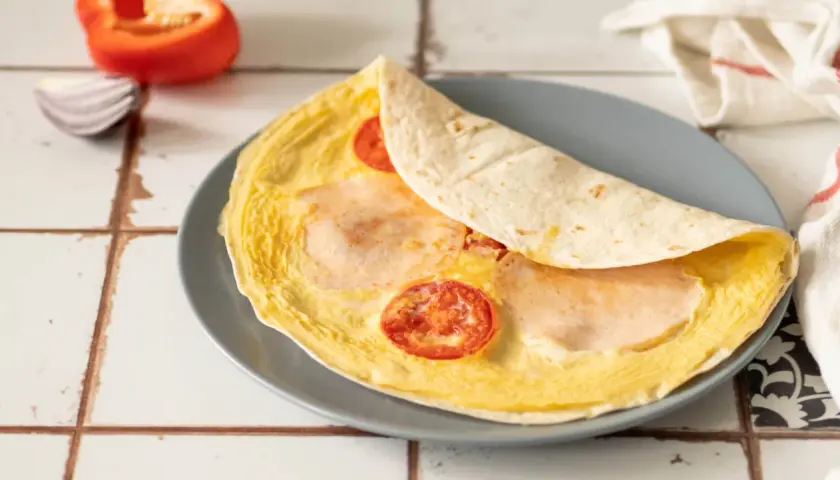 Pyszna tortilla z jajkiem, pomidorem i szynką, gotowa do zjedzenia.