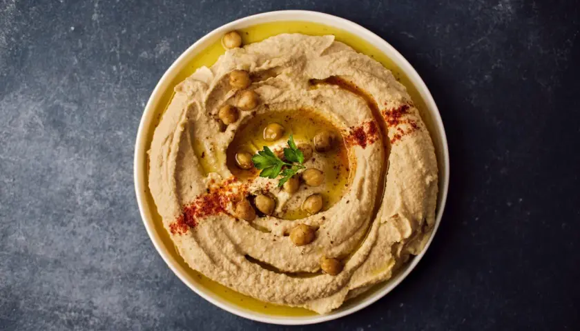 Cremoso hummus di ceci guarnito con ceci interi, paprika e prezzemolo, pronto per essere gustato.