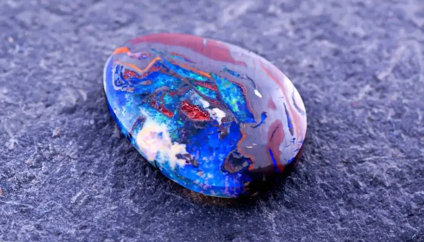 Ein faszinierender Edelstein aus Australien, ein Boulderopal, zeigt ein lebendiges Farbspiel aus Blau, Rot und Orange auf dunklem Grund.