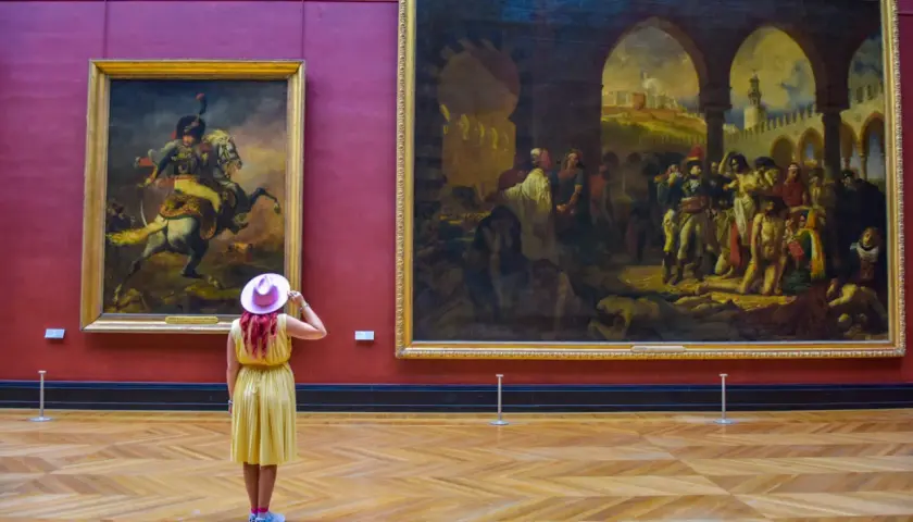 Kobieta w żółtej sukience i różowym kapeluszu podziwia obrazy w Luwrze. Co to za muzeum? To słynny paryski Luwr!