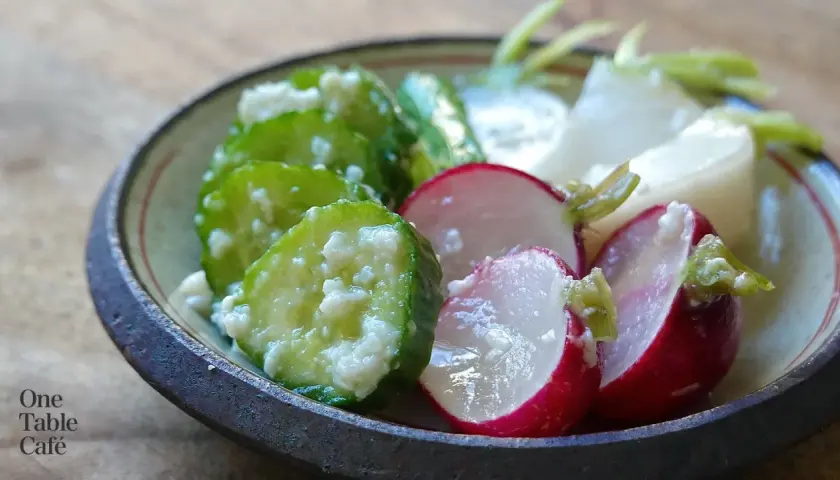 A close-up of a bowl filled with shio koji pickles. Sliced cucumbers and radishes are coated in a creamy marinade, showcasing their vibrant colors and textures.