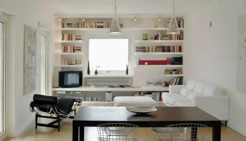 Librerie in cartongesso moderne con libri, TV, divano bianco e tavolo da pranzo.