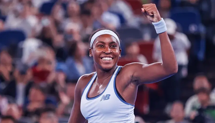 Uśmiechnięta gauff tenisistka z zaciśniętą pięścią w geście triumfu, na tle rozmazanej publiczności.