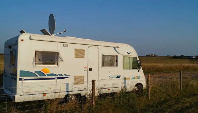 Camping-car blanc stationné dans un champ en Angleterre, avec Stonehenge à l'horizon.