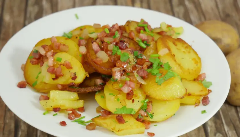 Bratkartoffeln mit gekochten Kartoffeln und Zwiebeln, garniert mit Speckwürfeln und Petersilie. Ein herzhaftes Gericht.