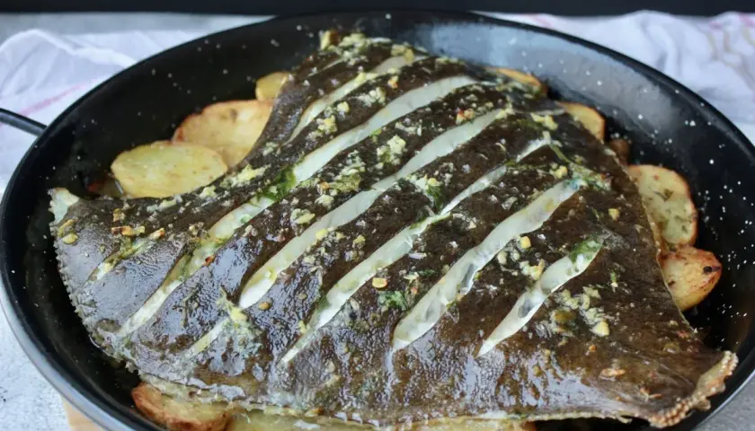 Rodaballo al horno con patatas, preparado con cortes y aderezado con hierbas y ajo.