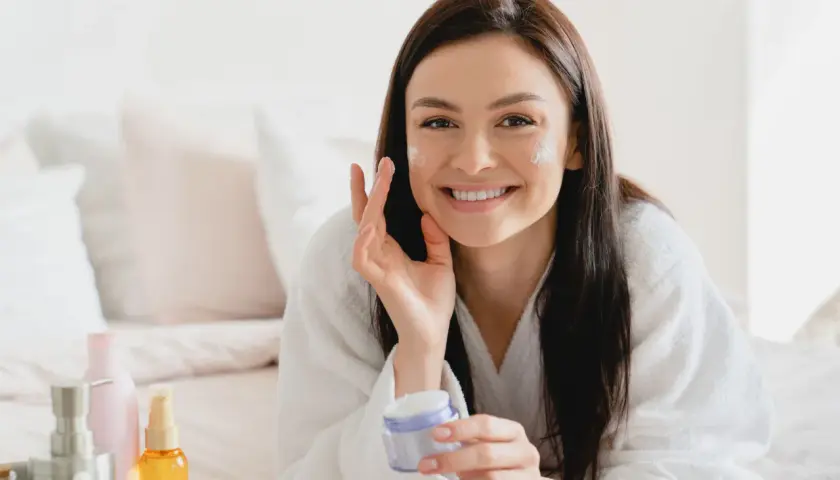 Donna sorridente applica crema viso, scoprendo i benefici di un siero probiotico per una pelle sana e luminosa.