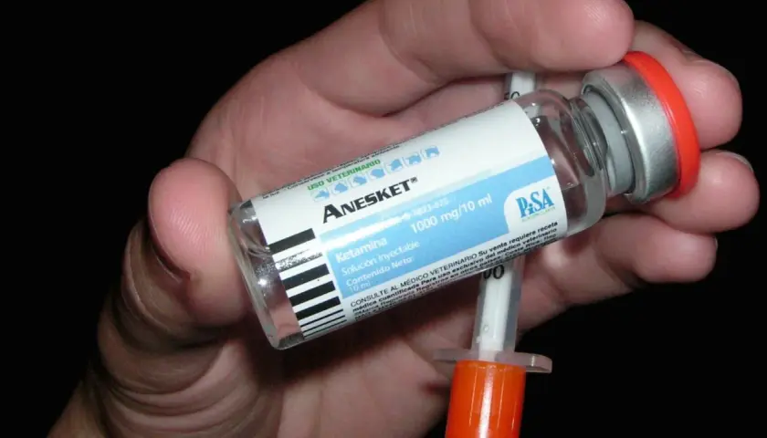 Mano che tiene una fiala di Anesket (ketamina) con siringa, suggerendo potenziali ketamina effetti positivi in contesti medici.