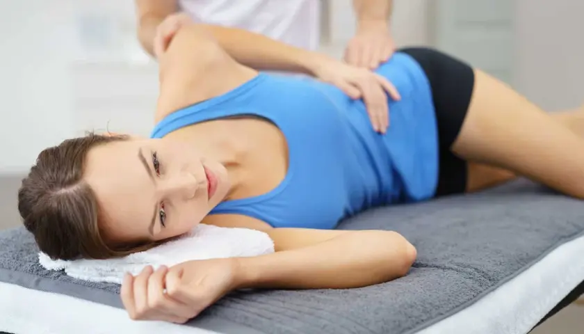 Fizjoterapeuta masuje kobietę z zapaleniem kaletki, łagodząc ból.