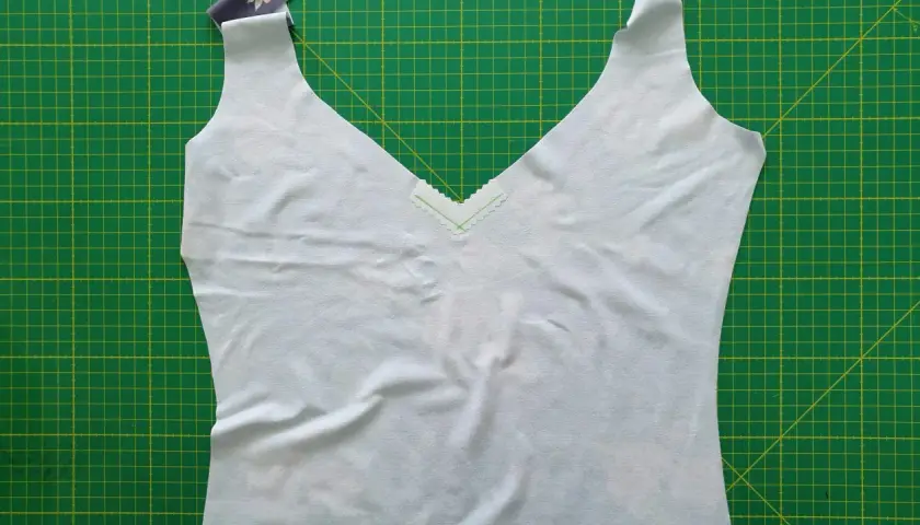 A light blue garment with a deep v neck neckline, trimmed with a delicate zigzag stitch, lies on a green cutting mat.