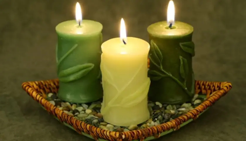 Tres velas verdes encendidas en un plato de mimbre con piedras. Encender velas en casa es malo, pero estas lucen tranquilas.