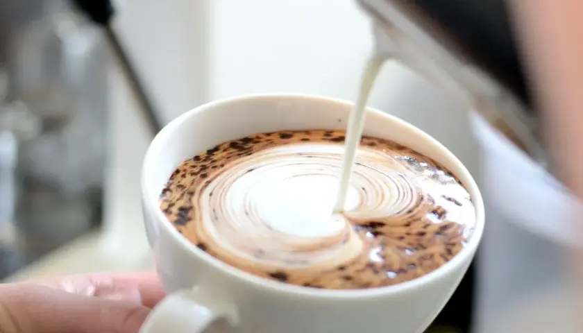 Barista wlewa mleko do kawy, tworząc wzór latte art.