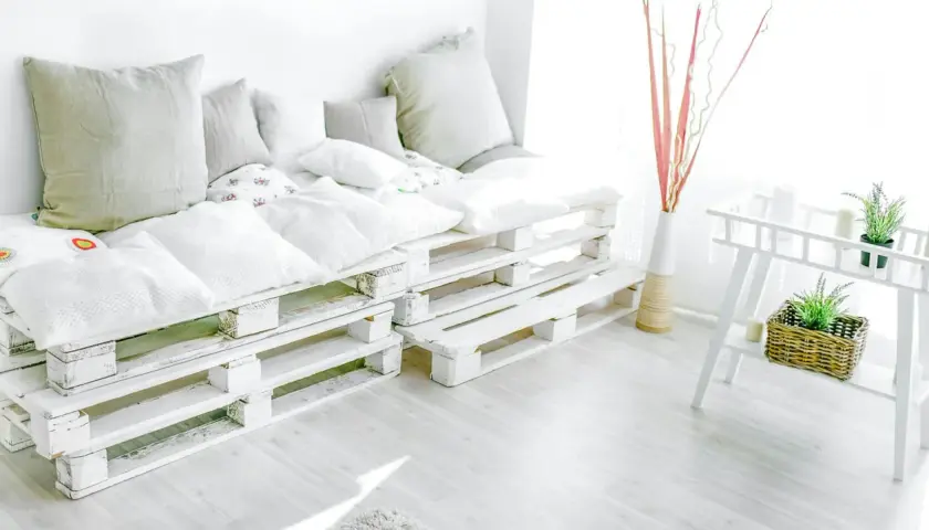 Wygodna kanapa z palet, czyli meble DIY. Jasne poduszki tworzą przytulną atmosferę.