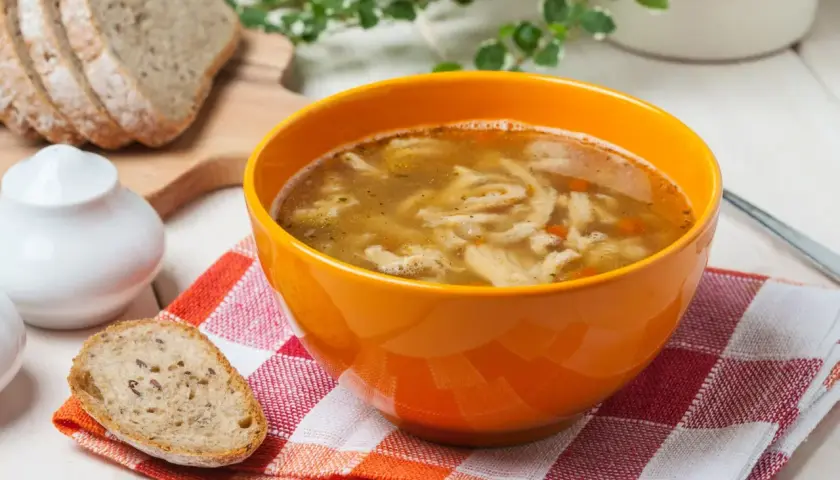 Gorąca zupa flaki w pomarańczowej misce, obok kromki chleba. Idealne do flaków są świeże dodatki.