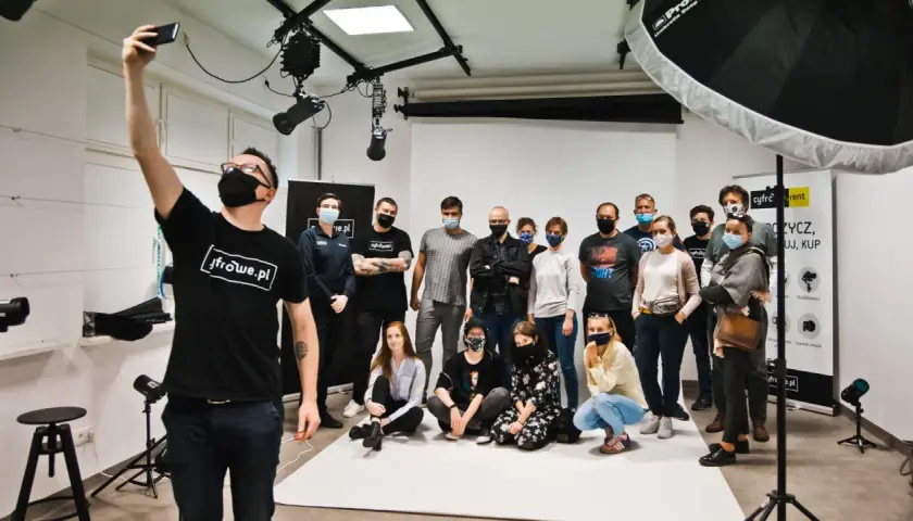 Grupa uczestników kursów foto w studiu, pozuje do wspólnego zdjęcia. Jeden z nich robi selfie.
