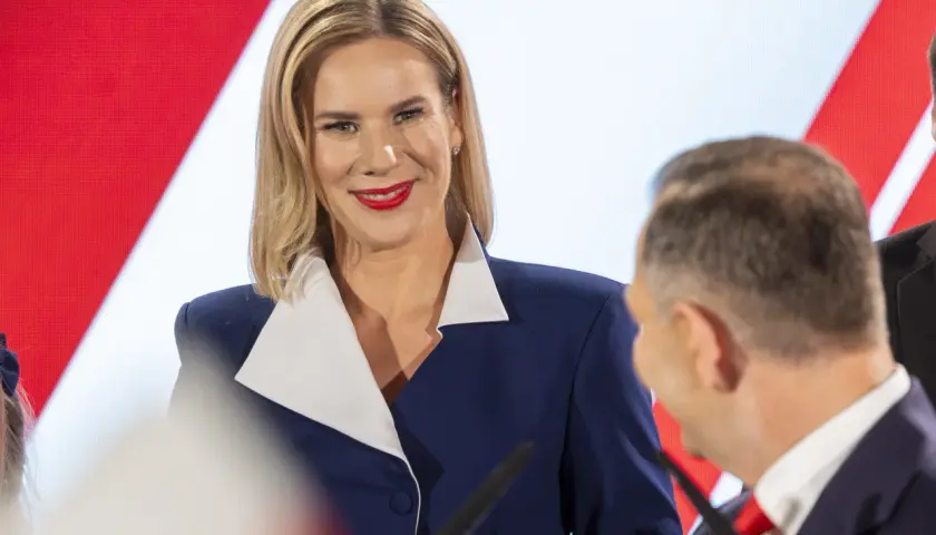 Kobieta w granatowej marynarce z białym kołnierzem uśmiecha się do mężczyzny.