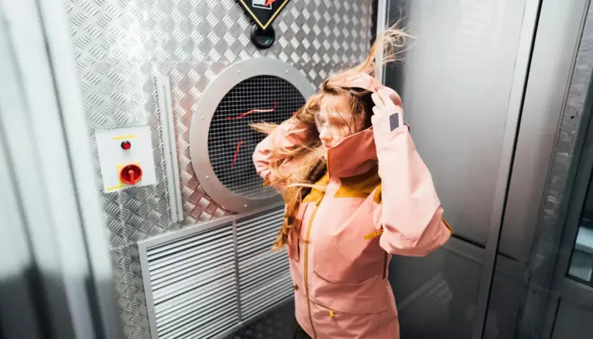 Dziewczyna w kurtce z materiału Gore-Tex co to jest, testuje jej odporność na wiatr w specjalnej komorze.