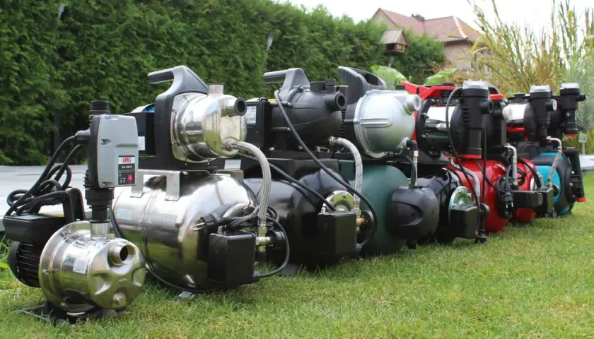 Reihe von Gartenpumpen und Hauswasserwerken auf einer grünen Wiese, bereit für den Einsatz im Garten.