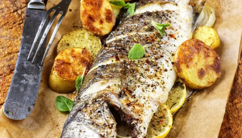 Trota salmonata al forno, dorata e saporita, servita con patate arrosto e limone. Un piatto invitante pronto da gustare.