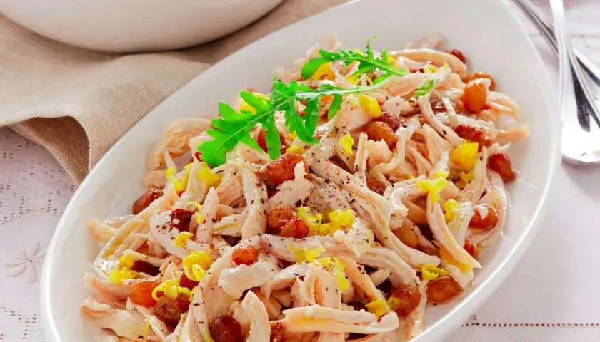 Insalata di pollo sfiziosa con uvetta e scorza di limone, guarnita con rucola fresca.