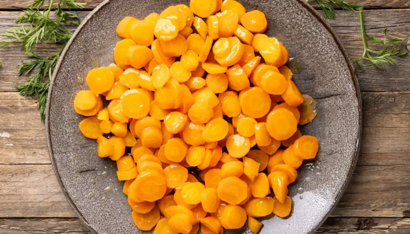 Carote bollite, tagliate a rondelle e disposte su un piatto grigio, con rametti di carota verde ai lati.